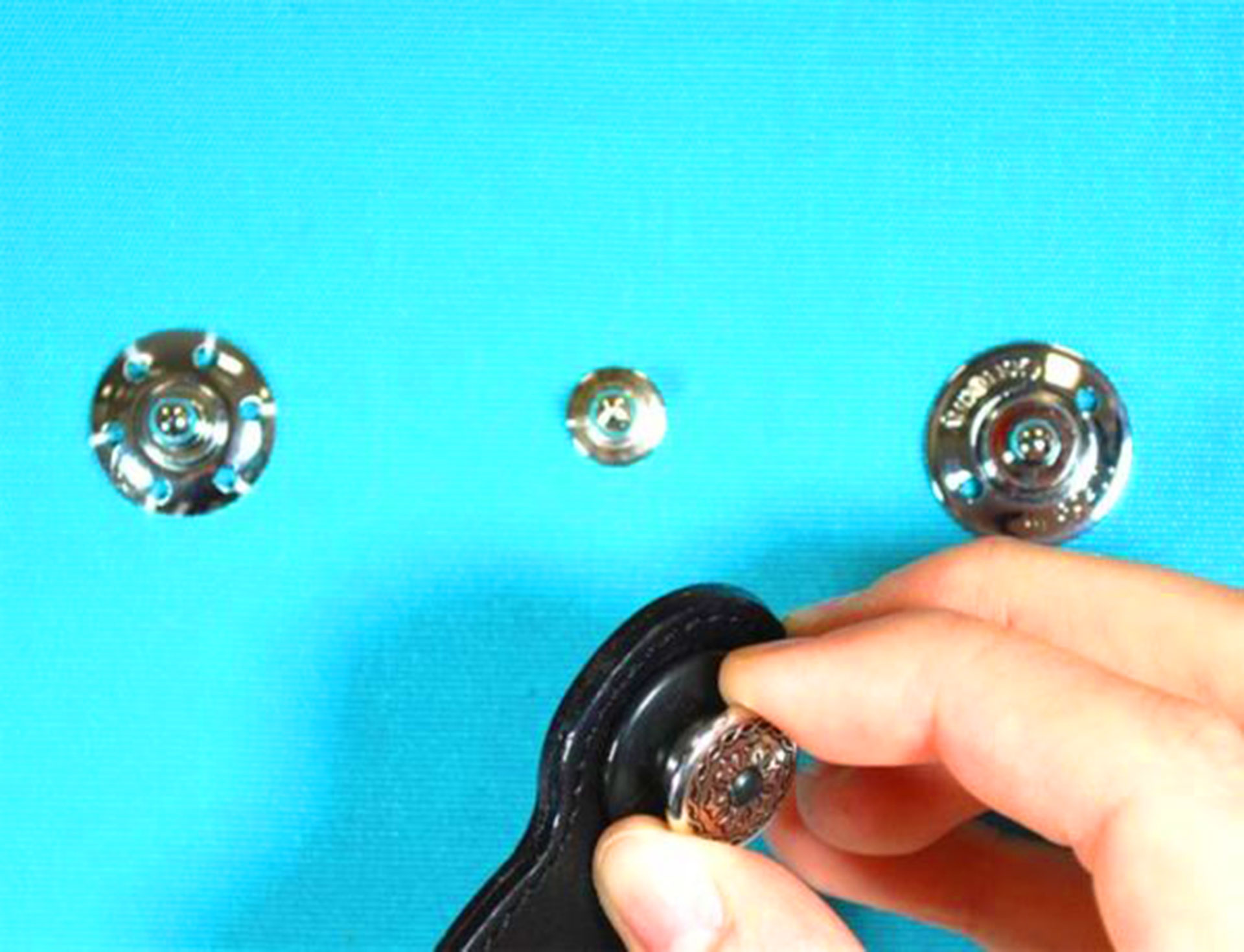 Hand attaching decorative snap fastener to black leather strap